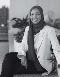 A smartly dressed business woman wearing a head covering and cream jacket.