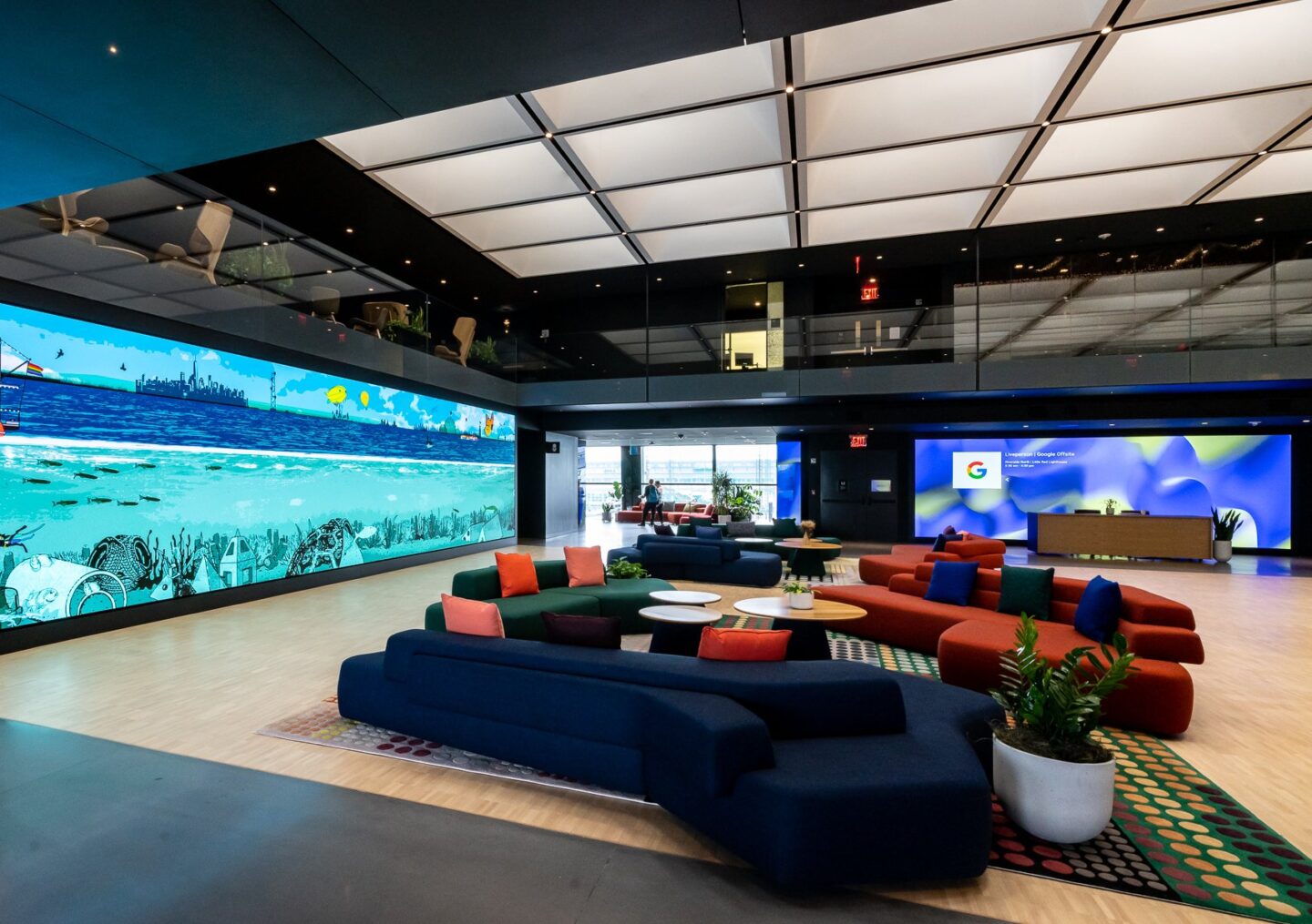 open lobby space in Google workplace with large digital screen wall and soft, colourful seating in the center and large skylight