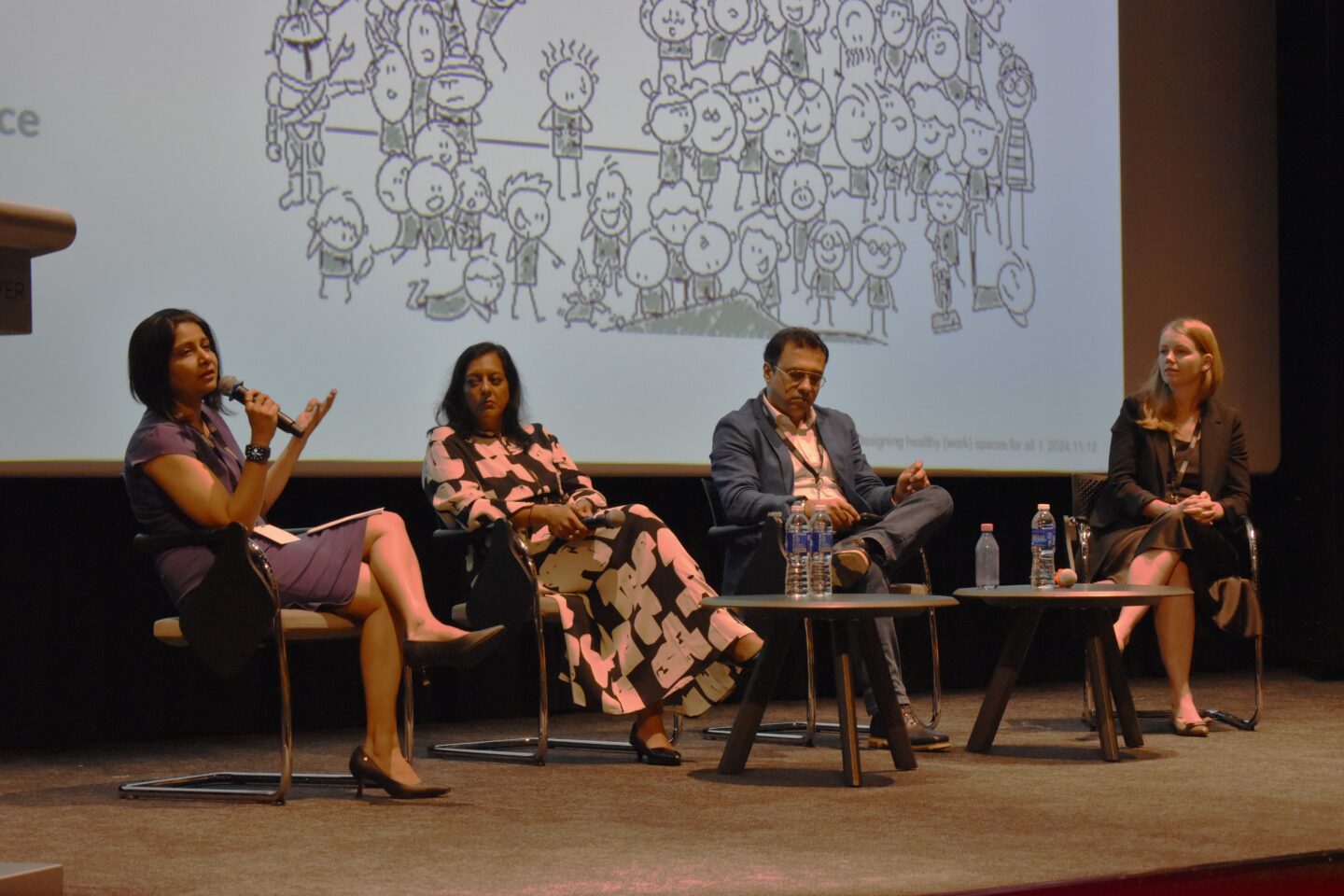 A panel of speakers seated on stage talking in front of a large white backdrop