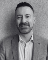 A bearded man wearing an open necked shirt and suit jacket