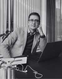 A man seated at a desk wearing a suit jacket