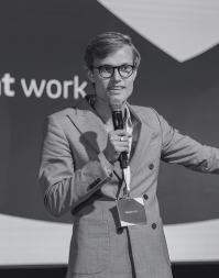 A man holding a microphone wearing a suite and delegate badge