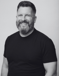 A bearded man with short hair wearing a dark coloured crew neck t-shirt.