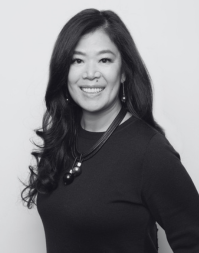 A woman with shoulder length brown hair wearing a dark coloured crew neck.