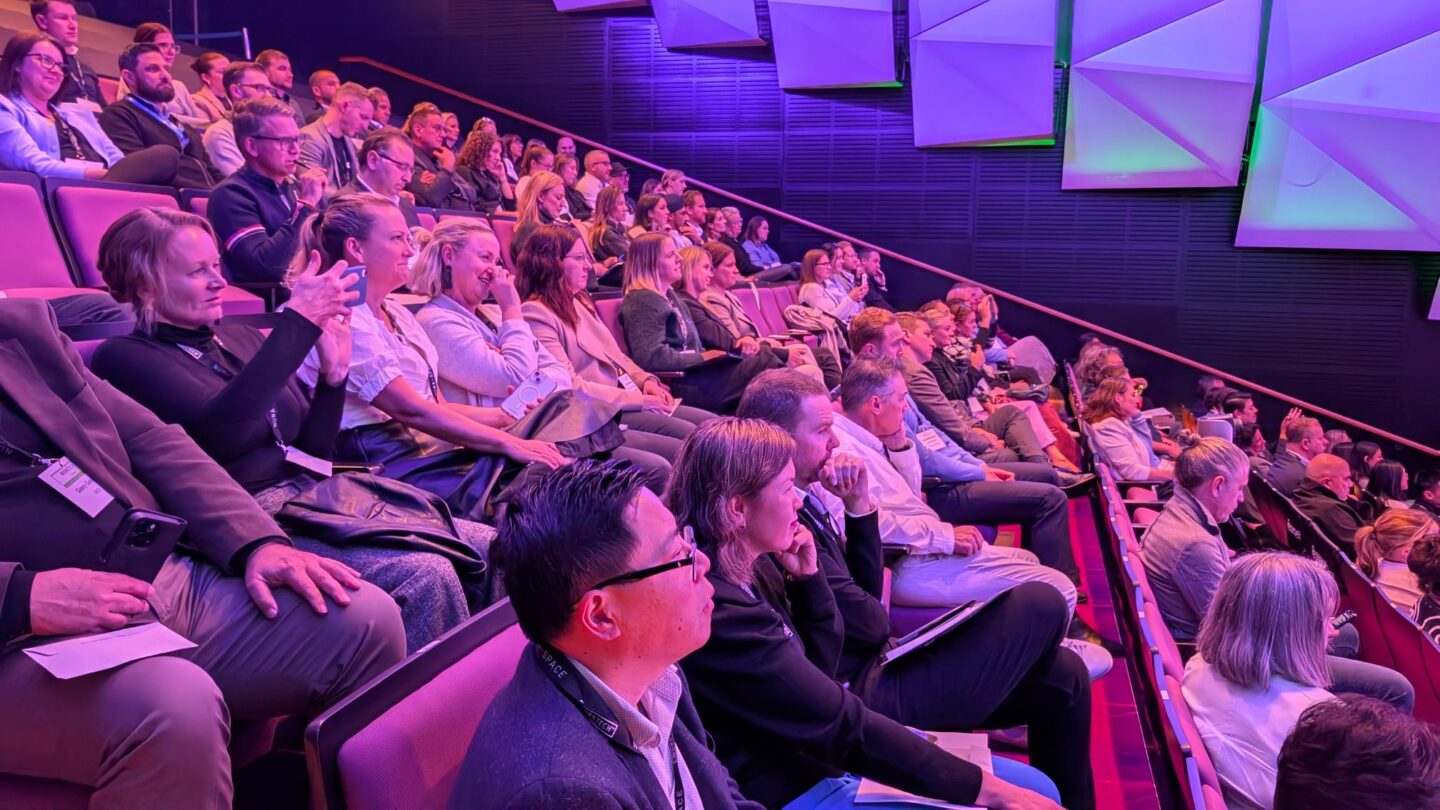 theatre style seating with a full audience in a dimly purple lite room