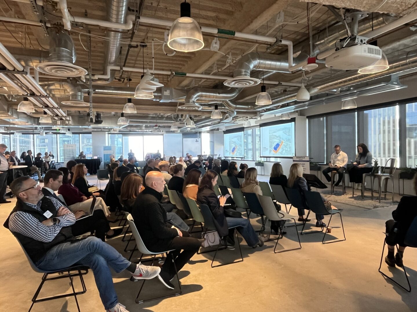 Speakers at WORKTECH Seattle sat on stage in front of a large seated audience in a brightly lit room